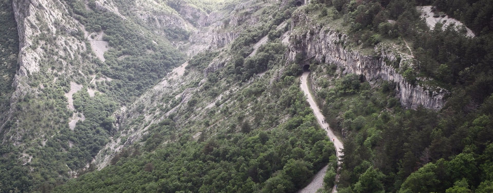 mountains landscape with road through a valley and pedaling cyclists mountains landscape with road through a valley and pedaling cyclists