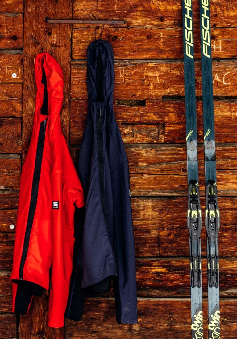 hanging ski clothes and a pair of cross-country skis leaning on the wall