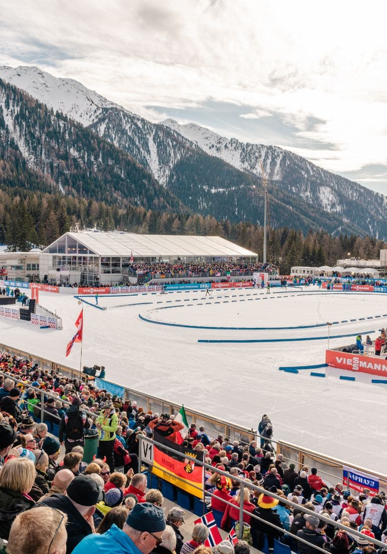 warm public in the stands of the Anterselva biathlon stadium in a snowy landscape